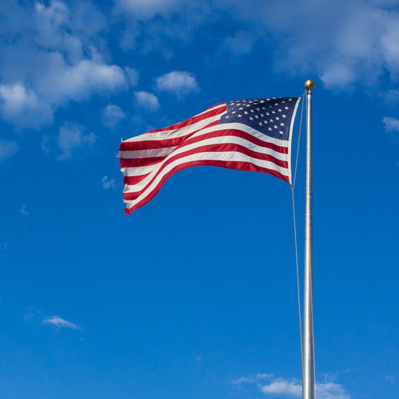 American flag - star and stripes floating over a cloudy blue sky