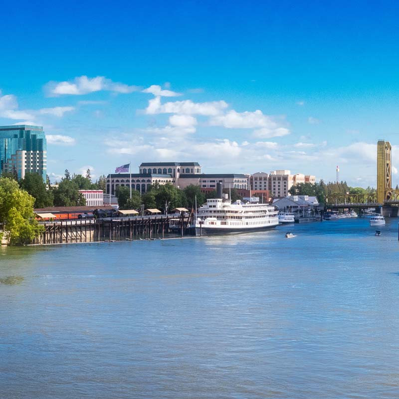 A panoramic view of Sacramento River near Old Town Sacramento, CA. A large ship is in the doc on the river near a bridge.